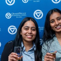 two girls smile in front of the GVSU Alumni backdrop